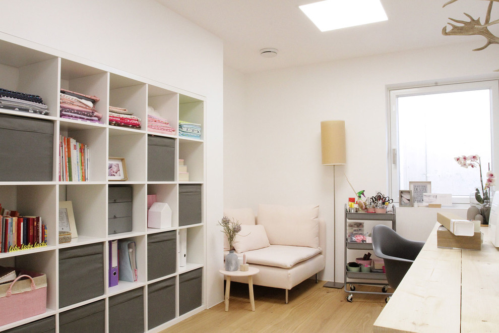Ejemplo de sala de manualidades actual con paredes blancas, suelo de madera en tonos medios y escritorio empotrado