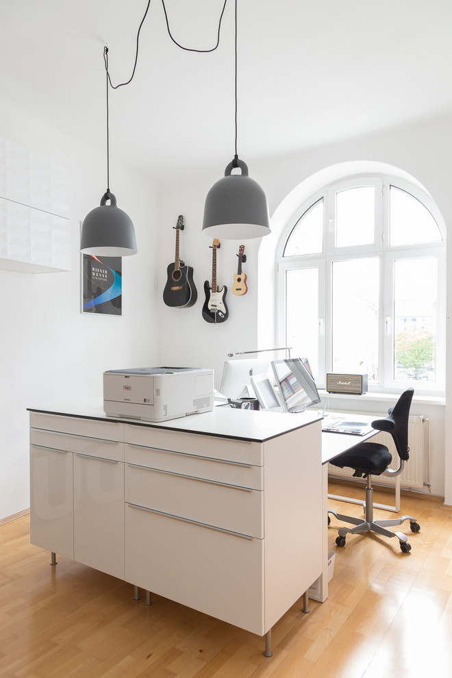 Modernes Arbeitszimmer mit weißer Wandfarbe, braunem Holzboden, freistehendem Schreibtisch und braunem Boden in Sonstige