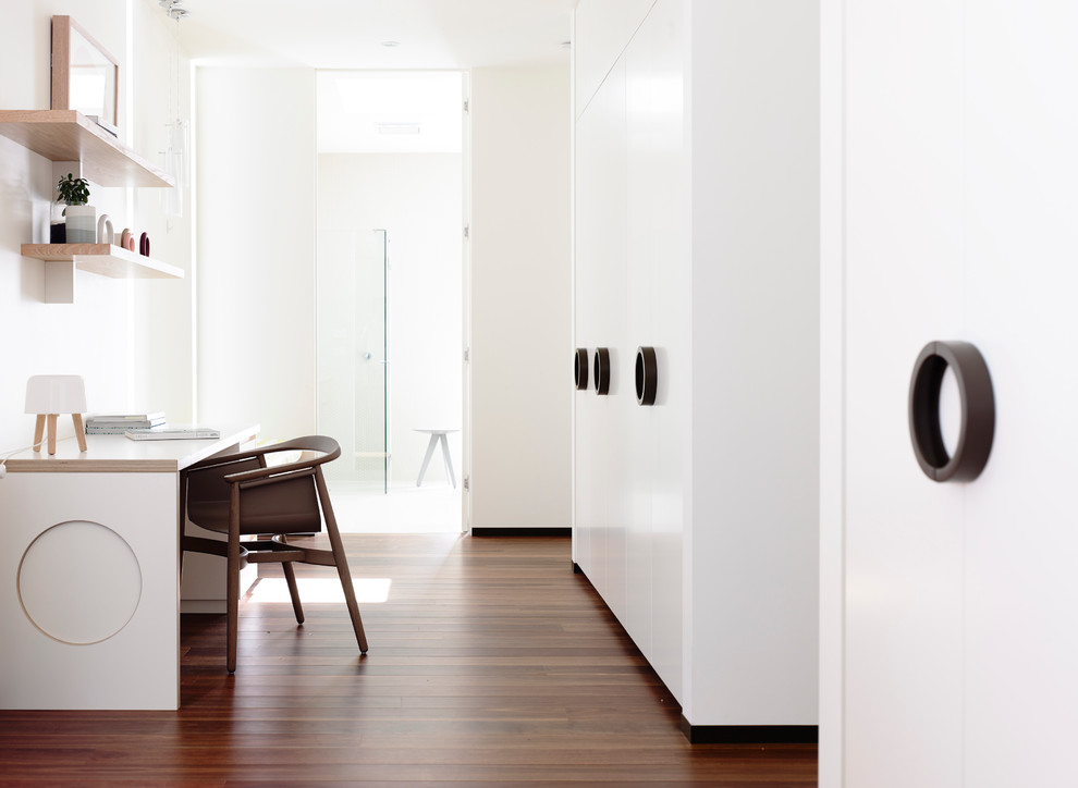 Cette image montre un bureau design avec un mur blanc, un sol en bois brun et un bureau intégré.