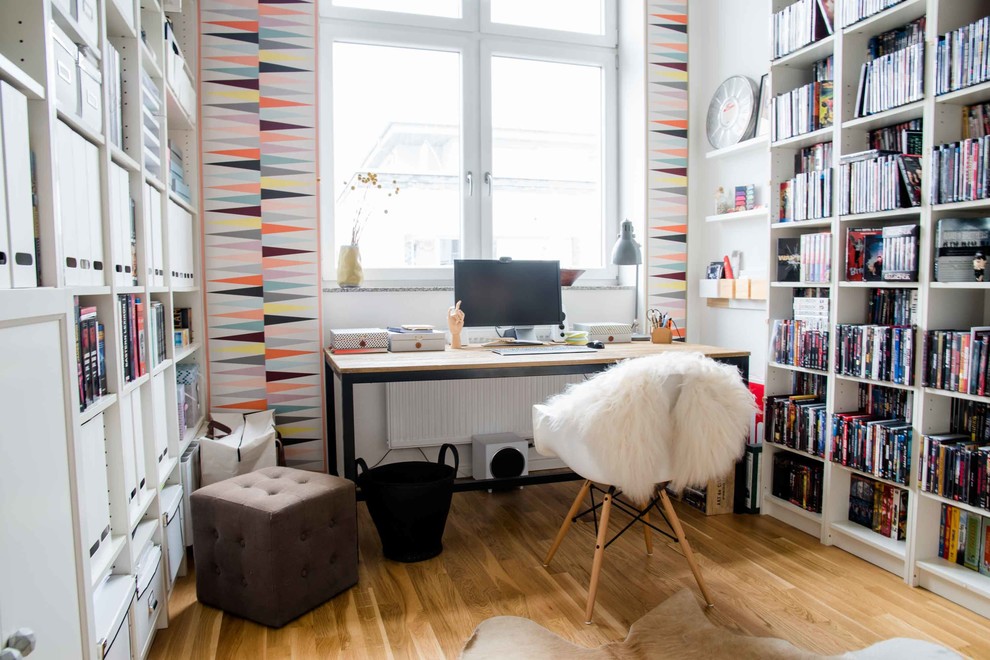Kleines Nordisches Arbeitszimmer ohne Kamin mit Arbeitsplatz, bunten Wänden, braunem Holzboden und freistehendem Schreibtisch in Berlin
