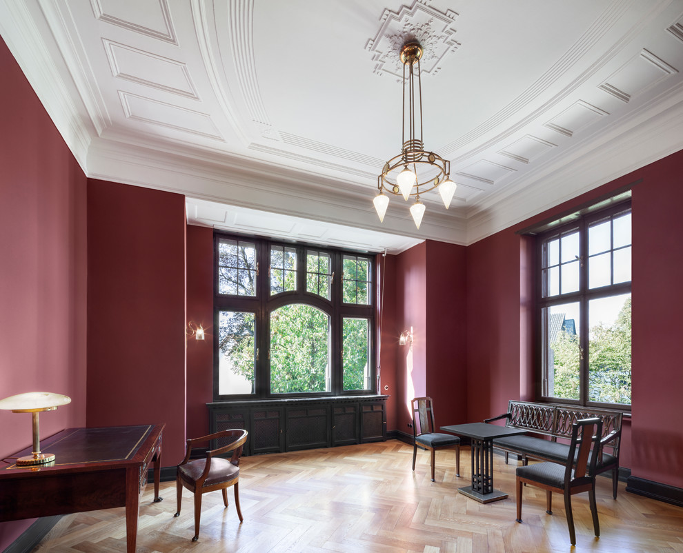 Imagen de despacho tradicional grande con paredes rojas, suelo de madera en tonos medios, escritorio independiente y suelo marrón