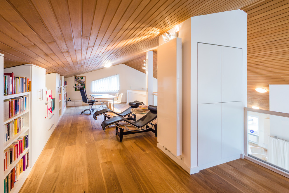 Geräumiges Modernes Lesezimmer ohne Kamin mit weißer Wandfarbe, braunem Holzboden, freistehendem Schreibtisch, verputzter Kaminumrandung und braunem Boden in Frankfurt am Main