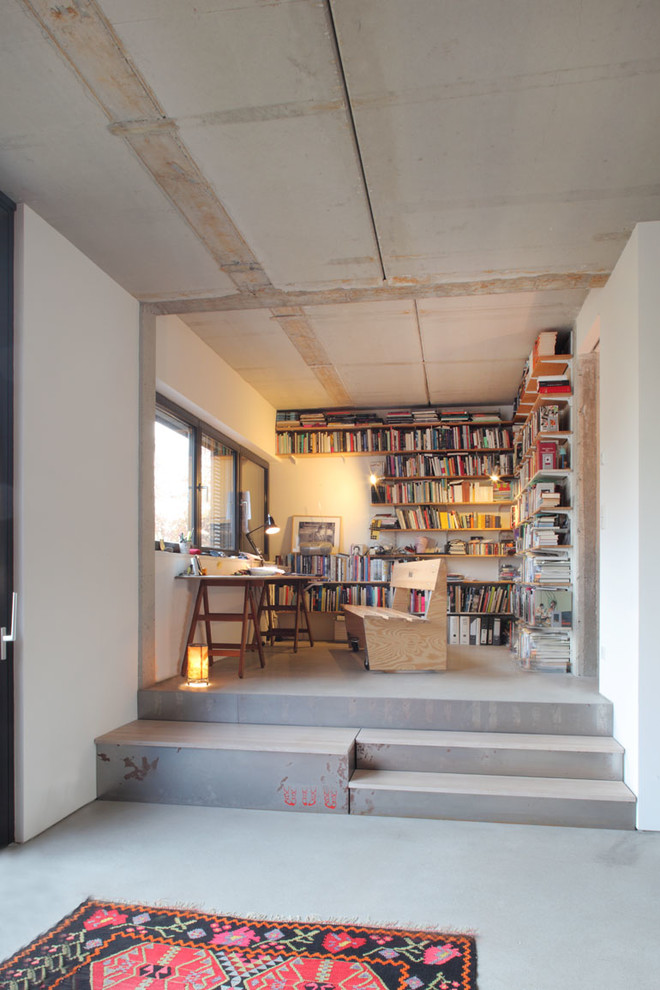 Foto di uno studio industriale di medie dimensioni con libreria, pareti bianche, pavimento in cemento, nessun camino, scrivania autoportante e pavimento grigio