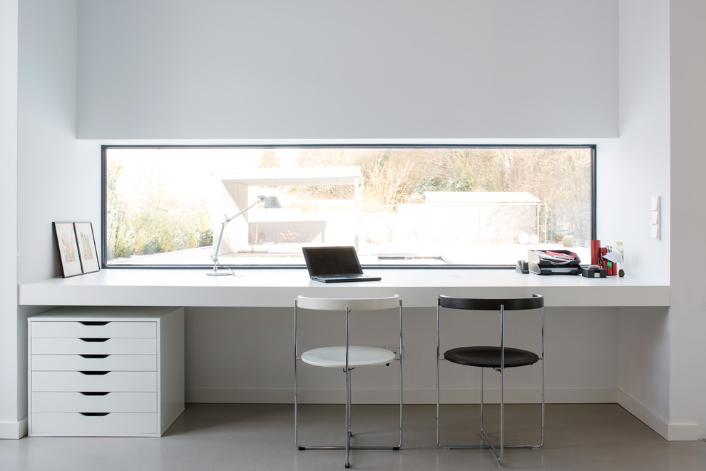 Diseño de despacho minimalista grande sin chimenea con paredes blancas, suelo de cemento y escritorio empotrado