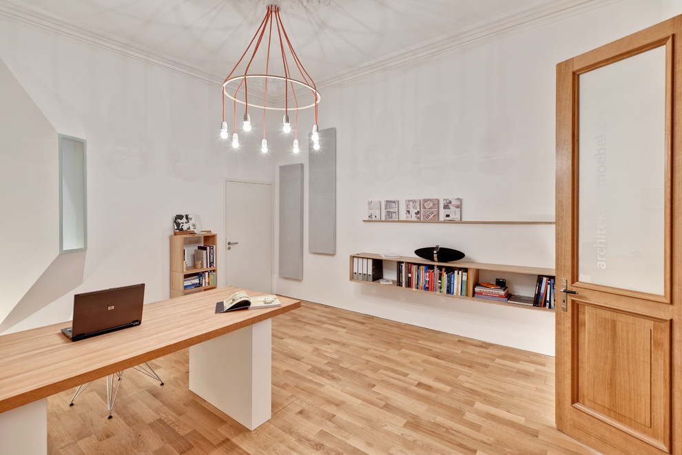 Foto på ett stort funkis hemmabibliotek, med vita väggar, ljust trägolv och ett fristående skrivbord