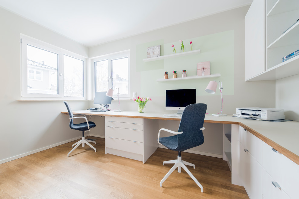 Modelo de despacho escandinavo grande sin chimenea con paredes beige, suelo de madera en tonos medios, escritorio empotrado y suelo marrón
