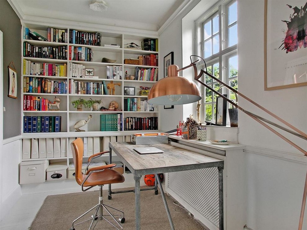Bild på ett mellanstort skandinaviskt hemmabibliotek, med vita väggar, målat trägolv och ett fristående skrivbord