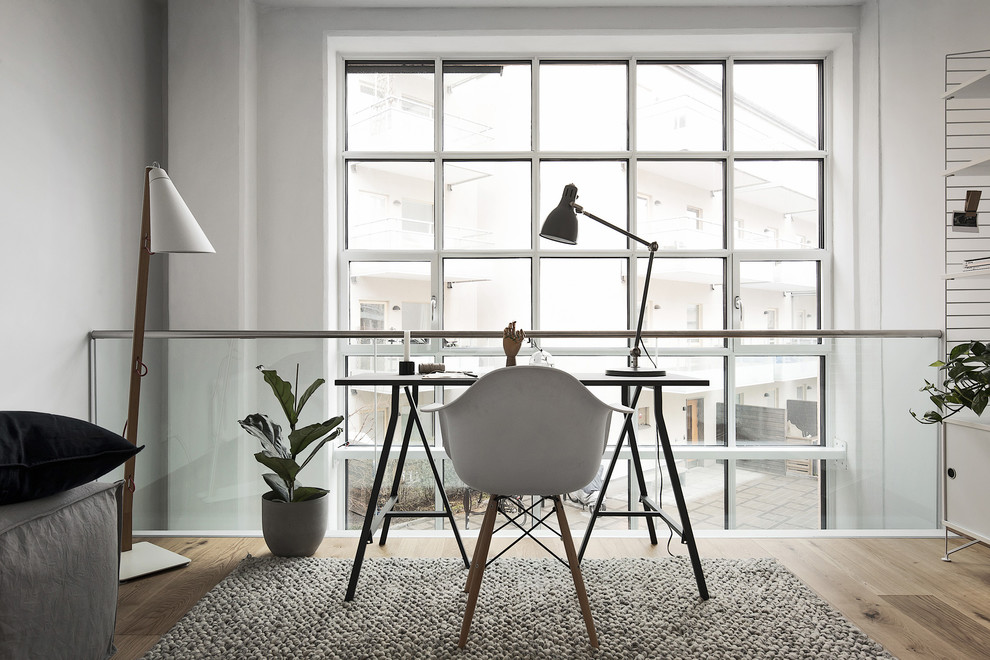 Nordisk inredning av ett litet arbetsrum, med vita väggar, mellanmörkt trägolv och ett fristående skrivbord