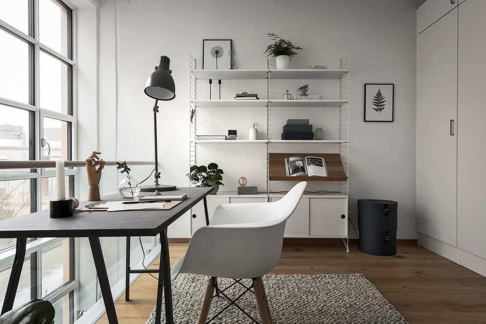Skandinavisk inredning av ett mellanstort arbetsrum, med vita väggar, mellanmörkt trägolv och ett fristående skrivbord