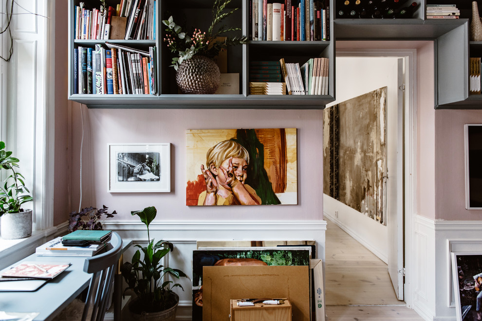 Bild på ett eklektiskt hemmabibliotek, med rosa väggar, ljust trägolv, ett fristående skrivbord och beiget golv