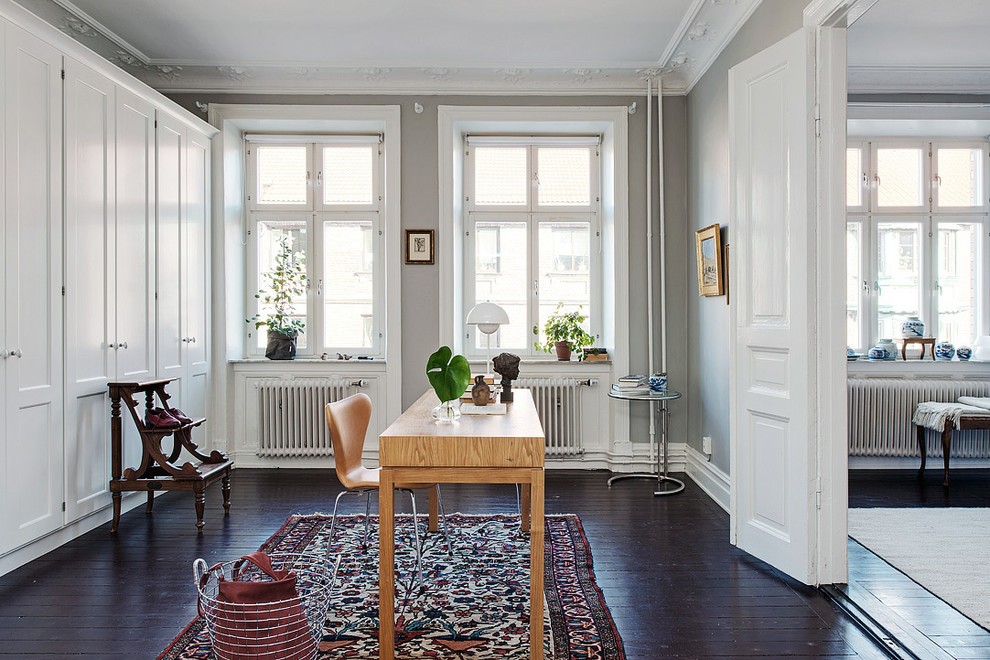На фото: рабочее место среднего размера в скандинавском стиле с серыми стенами, темным паркетным полом и отдельно стоящим рабочим столом без камина с