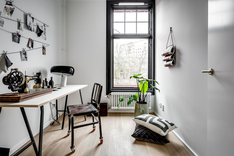 Medium sized industrial home office in Stockholm with white walls, light hardwood flooring, a freestanding desk and brown floors.
