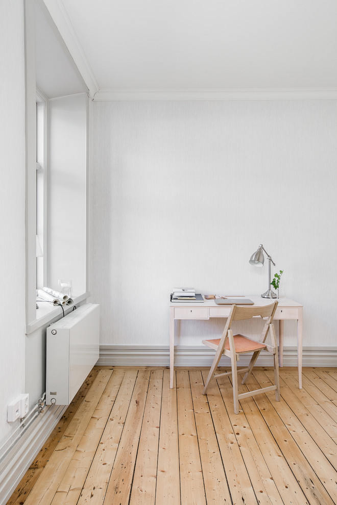 Diseño de despacho nórdico pequeño sin chimenea con paredes blancas, suelo de madera clara y escritorio independiente
