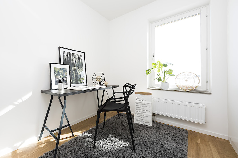 Immagine di uno studio scandinavo con pareti bianche, parquet chiaro, scrivania autoportante e pavimento marrone