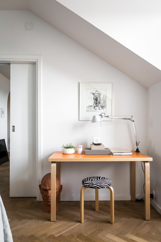 Стильный дизайн: рабочее место среднего размера в скандинавском стиле с белыми стенами, отдельно стоящим рабочим столом и светлым паркетным полом - последний тренд