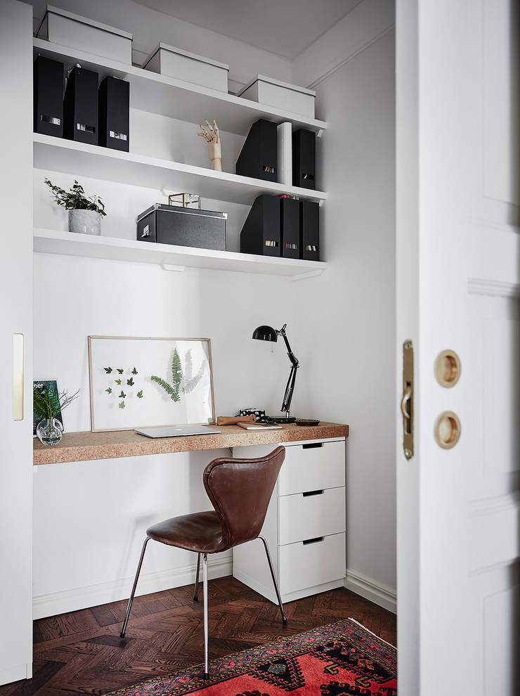 Danish built-in desk dark wood floor and brown floor home office photo in Gothenburg with white walls