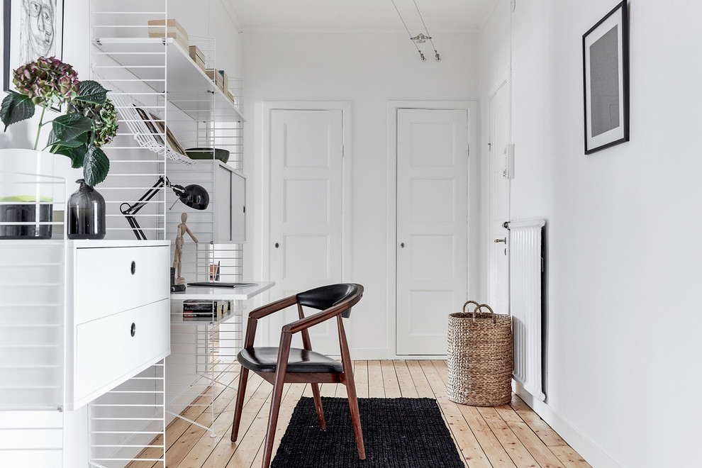 Foto på ett minimalistiskt hemmabibliotek, med vita väggar, ljust trägolv, ett inbyggt skrivbord och beiget golv
