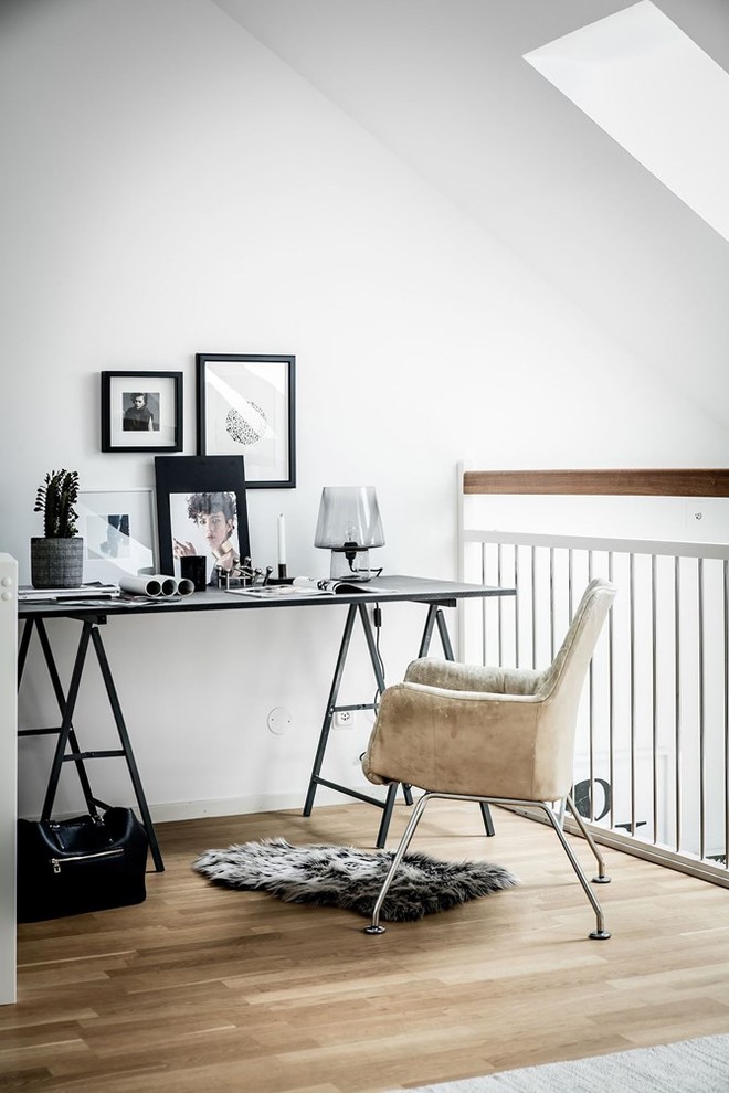 На фото: рабочее место в скандинавском стиле с белыми стенами, светлым паркетным полом, отдельно стоящим рабочим столом и бежевым полом с