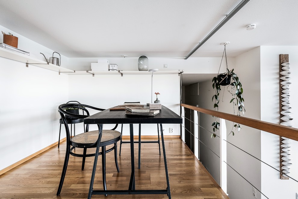 Bild på ett minimalistiskt arbetsrum, med vita väggar, mellanmörkt trägolv, ett fristående skrivbord och brunt golv