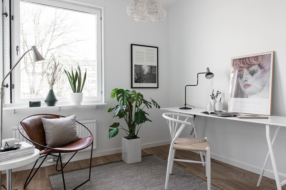 Medium sized scandinavian study in Gothenburg with white walls, medium hardwood flooring, no fireplace and a freestanding desk.