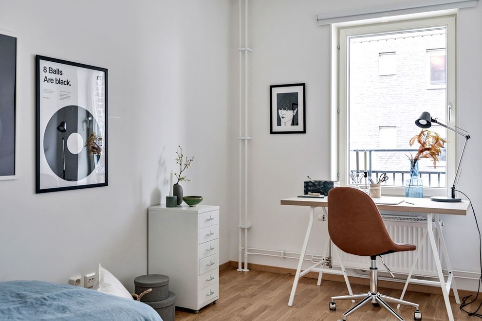 Minimalistisk inredning av ett arbetsrum, med vita väggar, mellanmörkt trägolv, ett fristående skrivbord och brunt golv