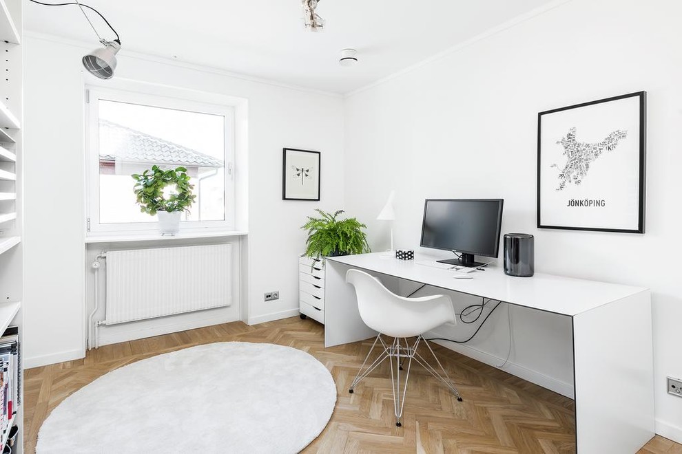 Skandinavisches Arbeitszimmer mit weißer Wandfarbe, braunem Holzboden und freistehendem Schreibtisch in Göteborg