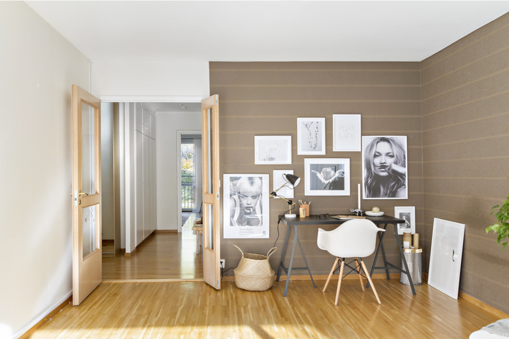 Imagen de estudio nórdico sin chimenea con paredes marrones, suelo de madera en tonos medios y escritorio independiente