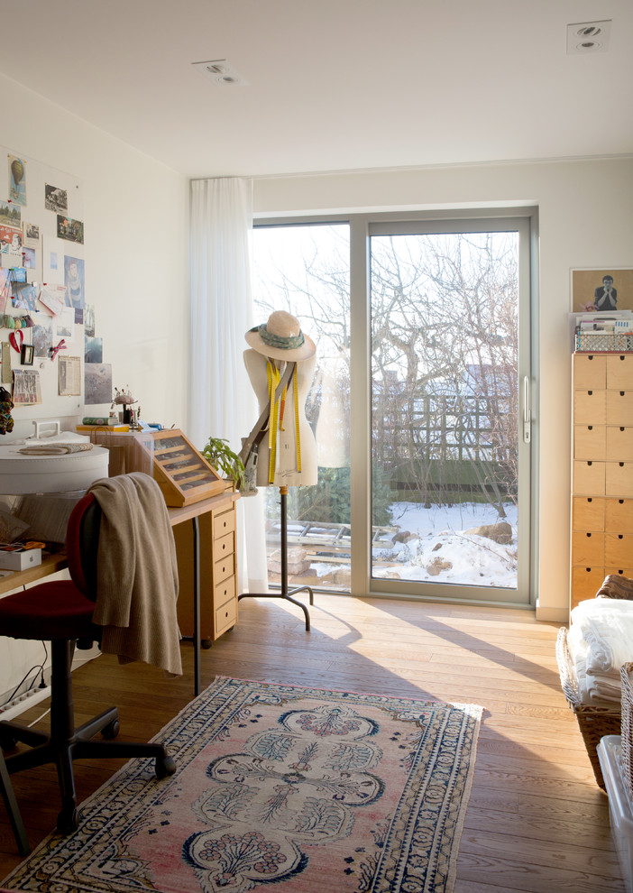 Photo of a scandi craft room in Stockholm with white walls, light hardwood flooring, a freestanding desk and beige floors.