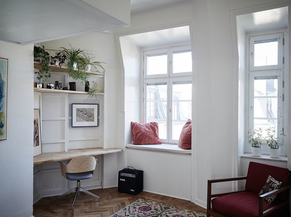 Inspiration för ett skandinaviskt hemmabibliotek, med vita väggar, mellanmörkt trägolv och ett inbyggt skrivbord