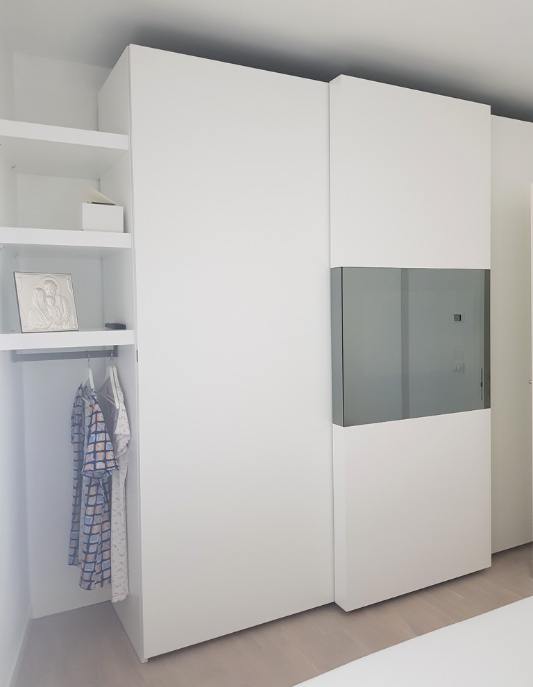 Photo of a medium sized modern gender neutral standard wardrobe in Milan with flat-panel cabinets, white cabinets, beige floors and light hardwood flooring.