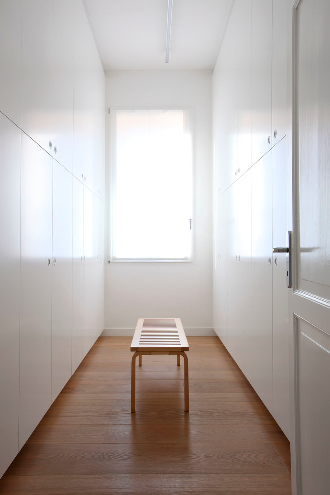 Photo of a modern wardrobe in Bologna with flat-panel cabinets, white cabinets and light hardwood flooring.