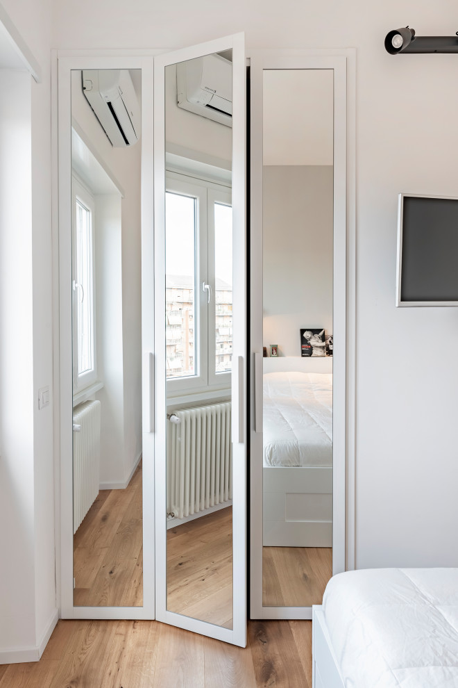 Imagen de armario vestidor unisex escandinavo pequeño con armarios tipo vitrina, puertas de armario blancas y suelo de madera clara
