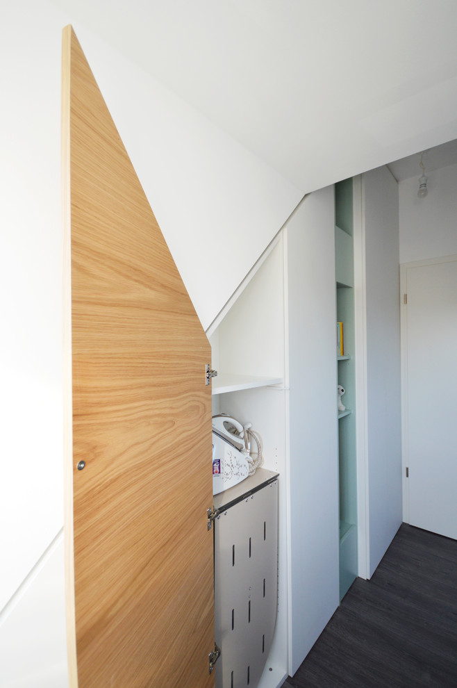 Ejemplo de armario unisex actual pequeño con suelo de madera oscura, suelo gris, armarios con paneles lisos y puertas de armario blancas