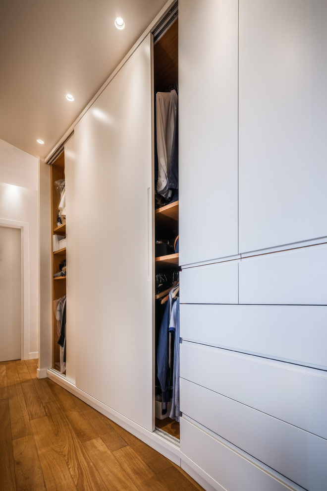 Esempio di un armadio o armadio a muro unisex minimal di medie dimensioni con ante lisce, ante bianche, pavimento in legno massello medio e pavimento marrone