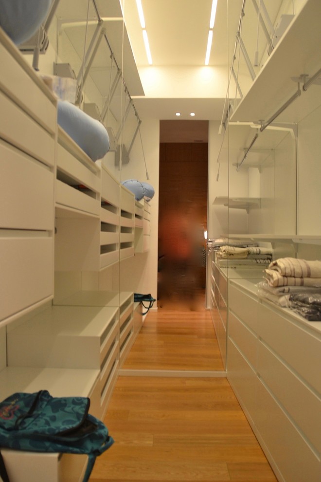 Immagine di una piccola cabina armadio unisex contemporanea con ante lisce, ante bianche e parquet chiaro