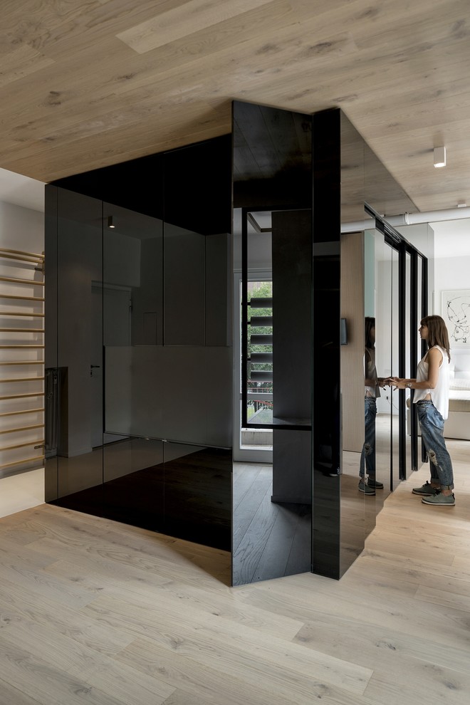 Aménagement d'un dressing contemporain avec un placard à porte plane, des portes de placard noires et parquet clair.