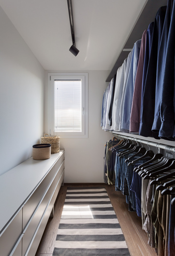 Modelo de armario vestidor unisex actual de tamaño medio con armarios con paneles lisos, puertas de armario grises, suelo de madera en tonos medios y suelo marrón