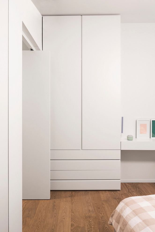 Imagen de armario y vestidor unisex moderno con armarios con paneles lisos, puertas de armario blancas y suelo de madera en tonos medios