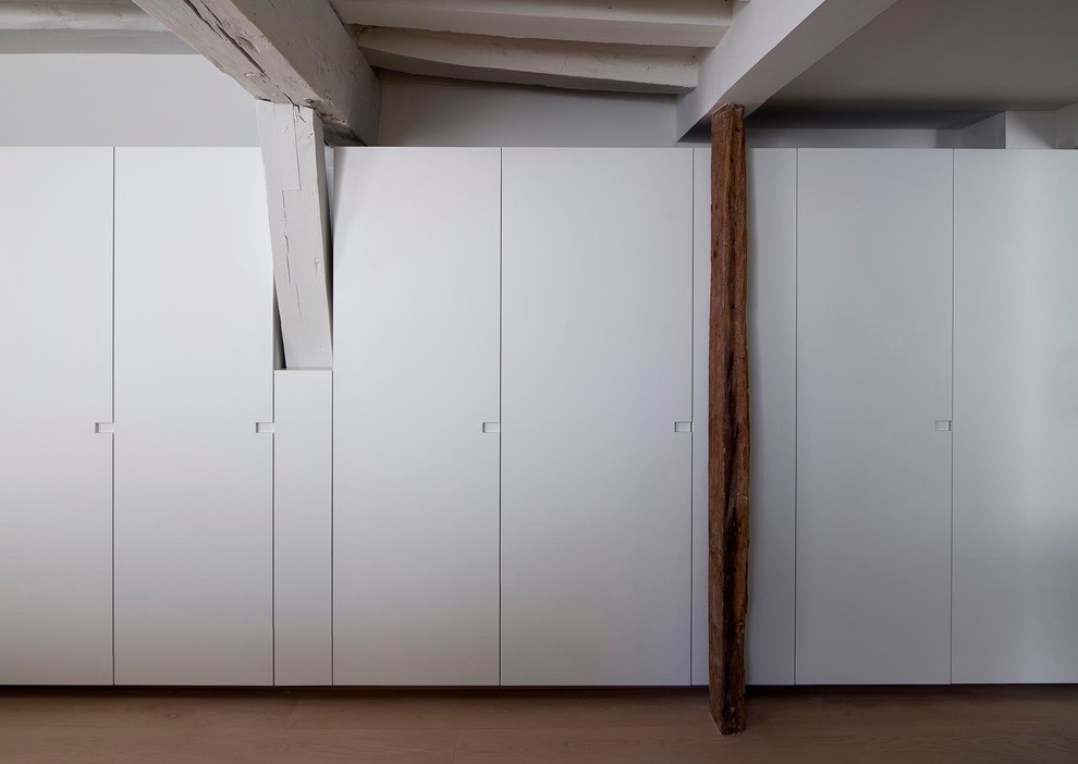 Aménagement d'un grand placard dressing contemporain neutre avec un placard à porte plane, des portes de placard blanches et un sol en bois brun.