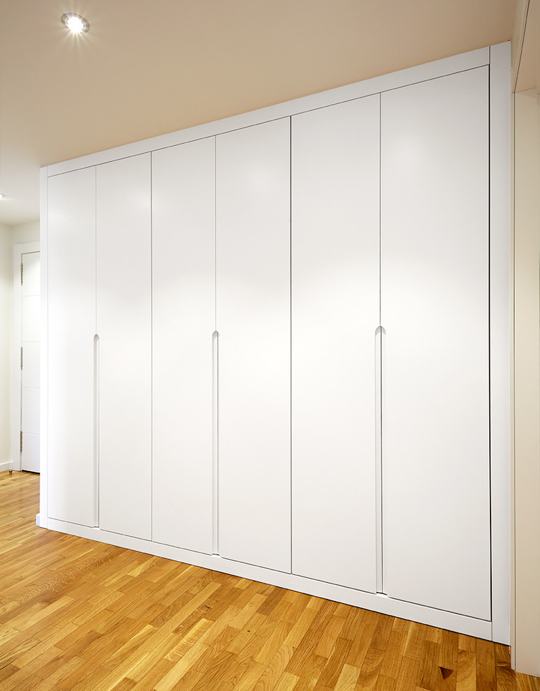Diseño de armario unisex tradicional renovado de tamaño medio con armarios con paneles lisos, puertas de armario blancas y suelo de madera en tonos medios