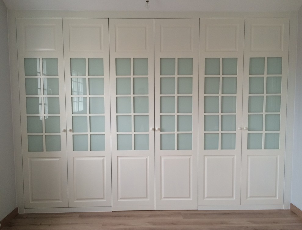 Modelo de armario unisex tradicional renovado de tamaño medio con armarios tipo vitrina, puertas de armario blancas y suelo de madera en tonos medios