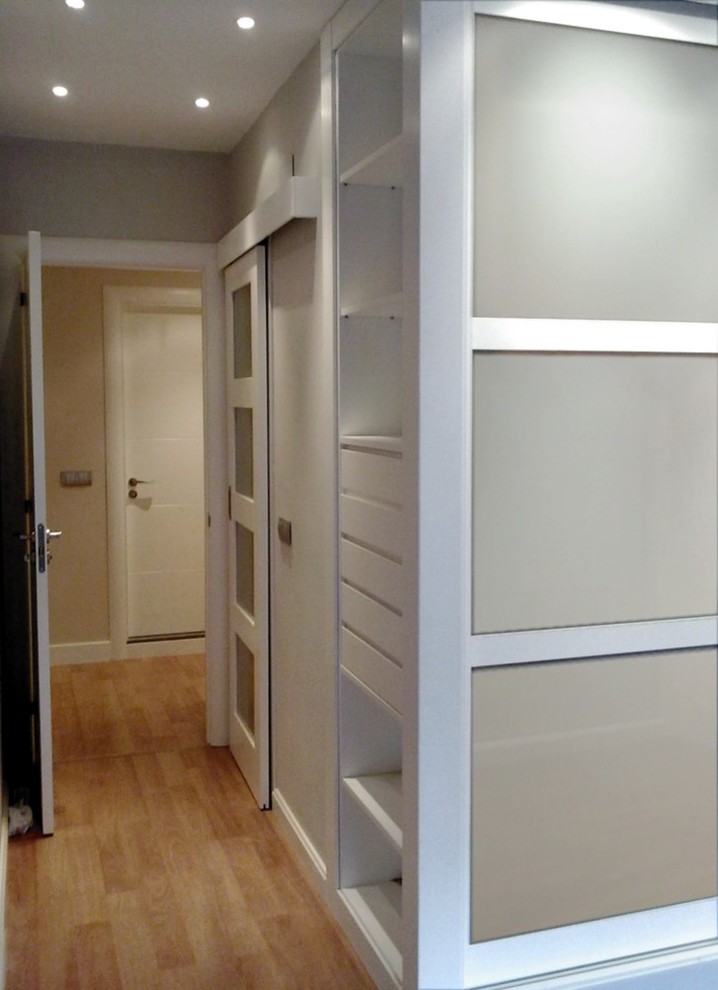 Diseño de armario vestidor unisex actual de tamaño medio con puertas de armario blancas y suelo de madera en tonos medios