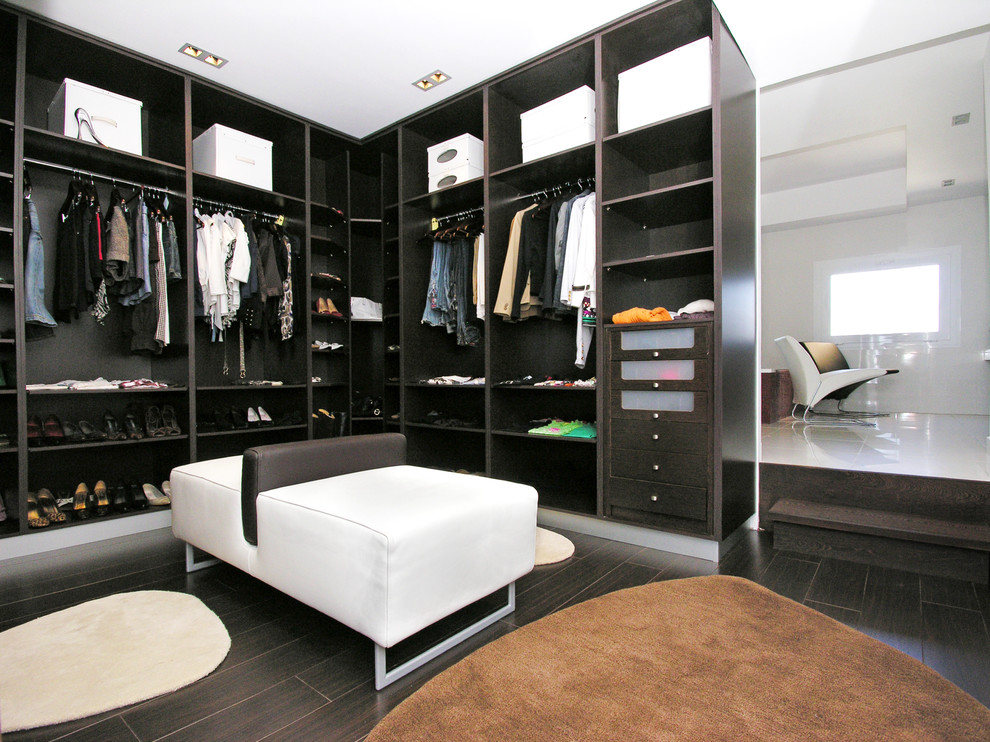 Ejemplo de vestidor unisex actual de tamaño medio con armarios abiertos, puertas de armario negras, suelo marrón y suelo de madera oscura