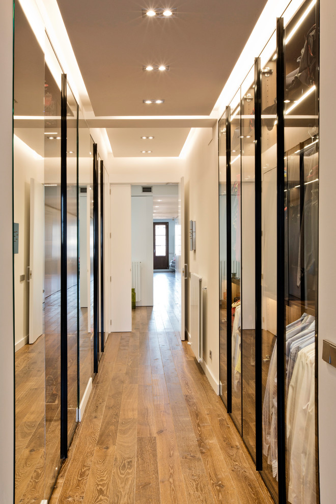 Inspiration for a large contemporary gender neutral walk-in wardrobe in Barcelona with glass-front cabinets, medium hardwood flooring and brown floors.