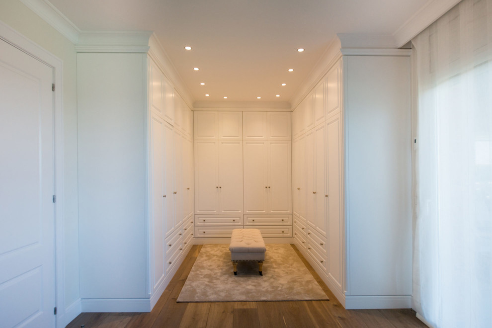 Exemple d'un grand dressing room chic neutre avec des portes de placard blanches et un sol en bois brun.