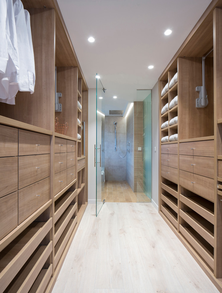 Diseño de armario vestidor unisex actual grande con armarios abiertos, puertas de armario de madera oscura, suelo de madera clara y suelo beige