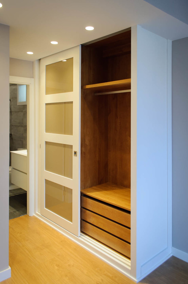 Imagen de armario y vestidor unisex actual de tamaño medio con armarios tipo vitrina, puertas de armario blancas y suelo de madera en tonos medios