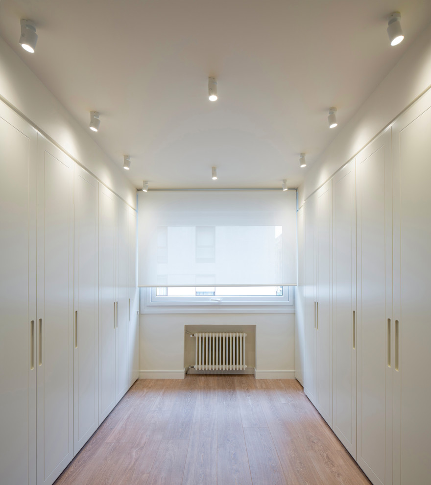 Foto de armario vestidor unisex nórdico grande con armarios con paneles lisos, puertas de armario blancas, suelo laminado y suelo marrón