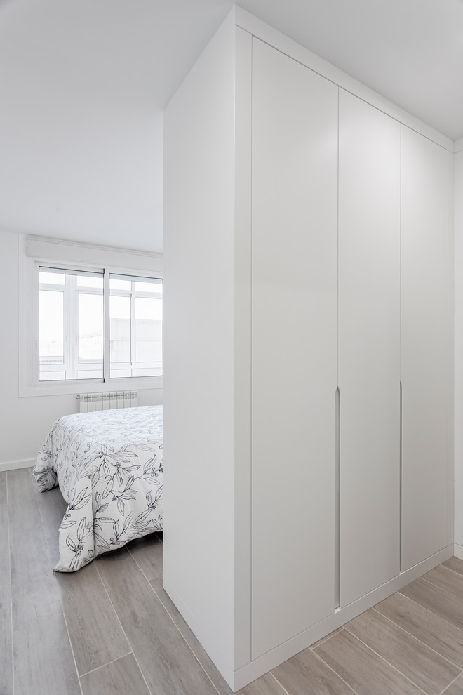 Modelo de armario vestidor actual pequeño con armarios con paneles lisos, puertas de armario blancas, suelo de baldosas de cerámica y suelo marrón