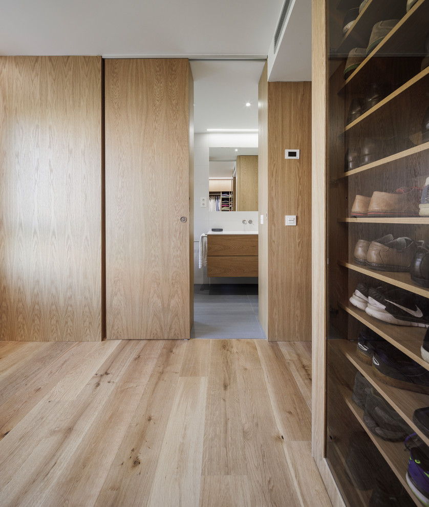 Moderner Begehbarer Kleiderschrank mit hellbraunen Holzschränken und braunem Holzboden in Madrid
